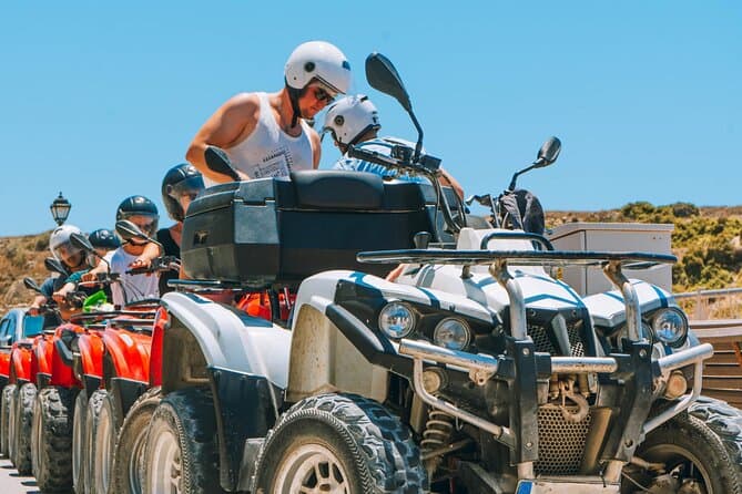Riders on quad bikes following a dusty coastal track across Gozo, Malta, with limestone hills behind them.
